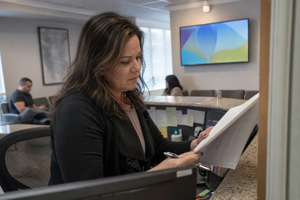 Practice manager reviewing a signage service contract at the front desk with the waiting room screen behind her